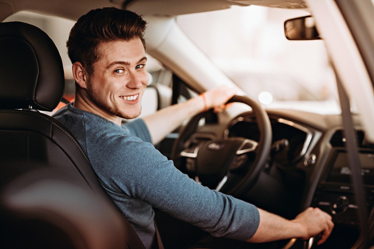 man in car smiling at camera with hand on shifter