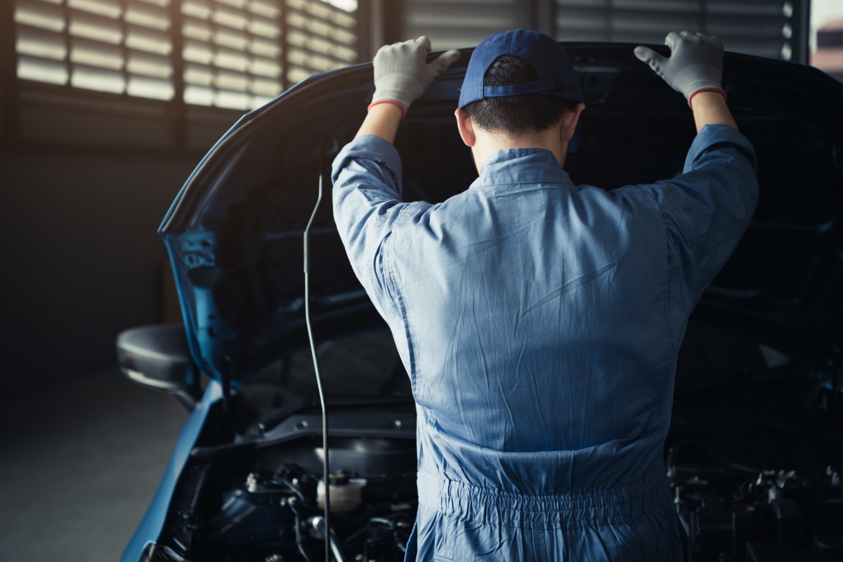 mechanic with hood up and looking at car